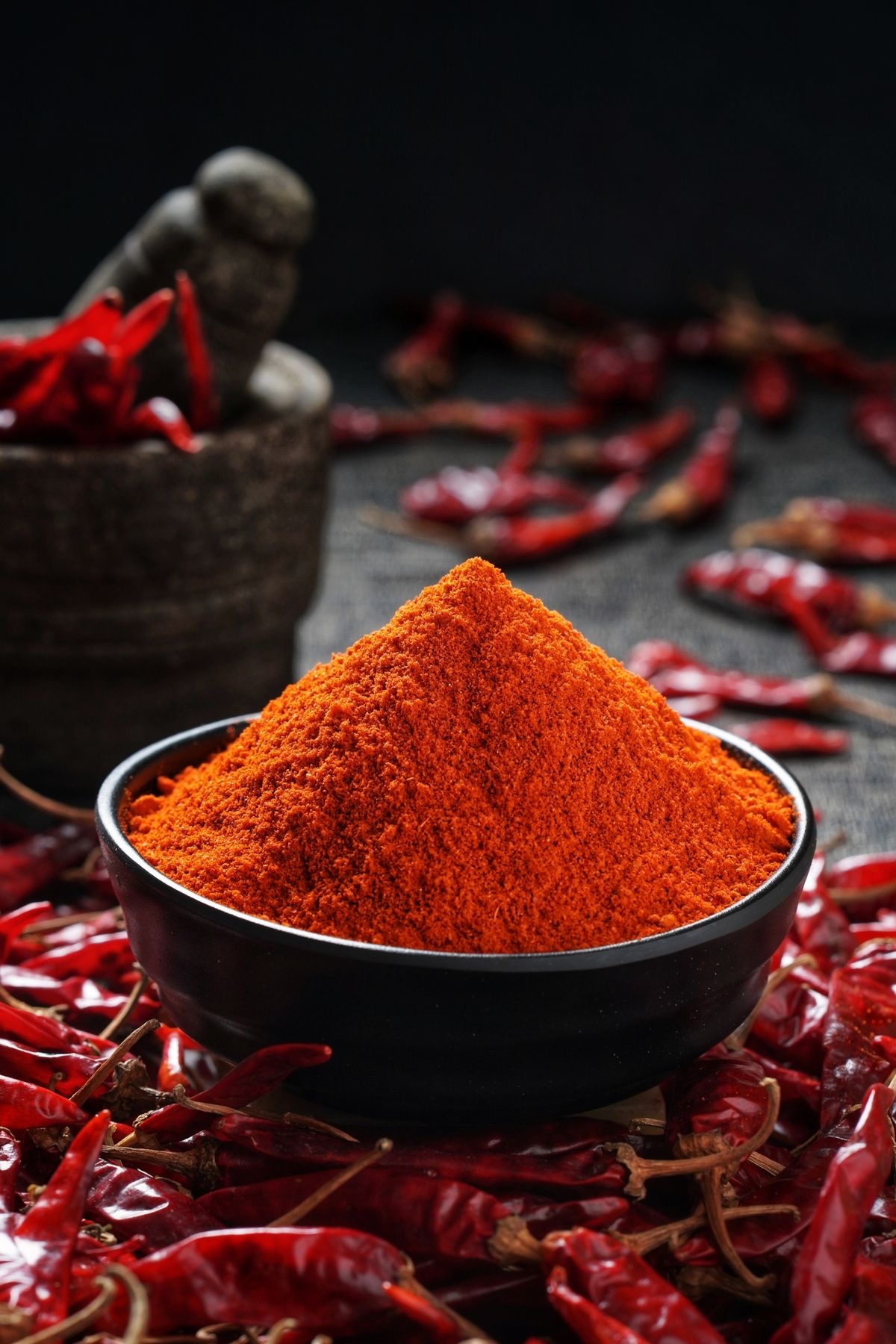 Red chilli powder in a black bowl with dried chillies
